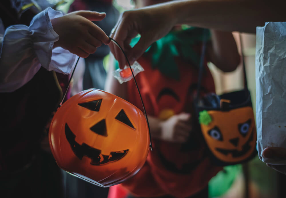 Children trick-or-treating in Manitoba holding pumpkin-shaped candy buckets while receiving Halloween treats from homeowners, TLR Law explains homeowner liability and safety tips in Manitoba.