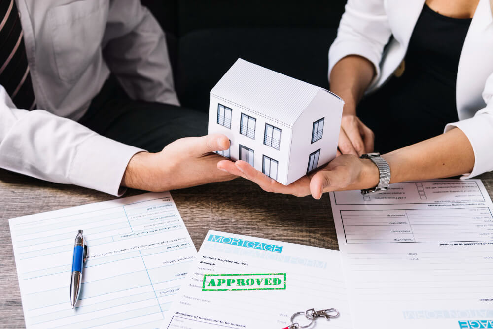 Hands exchanging a small house model over estate paperwork and an approved mortgage form, representing executor responsibilities and probate guidance from TLR Law in Manitoba.