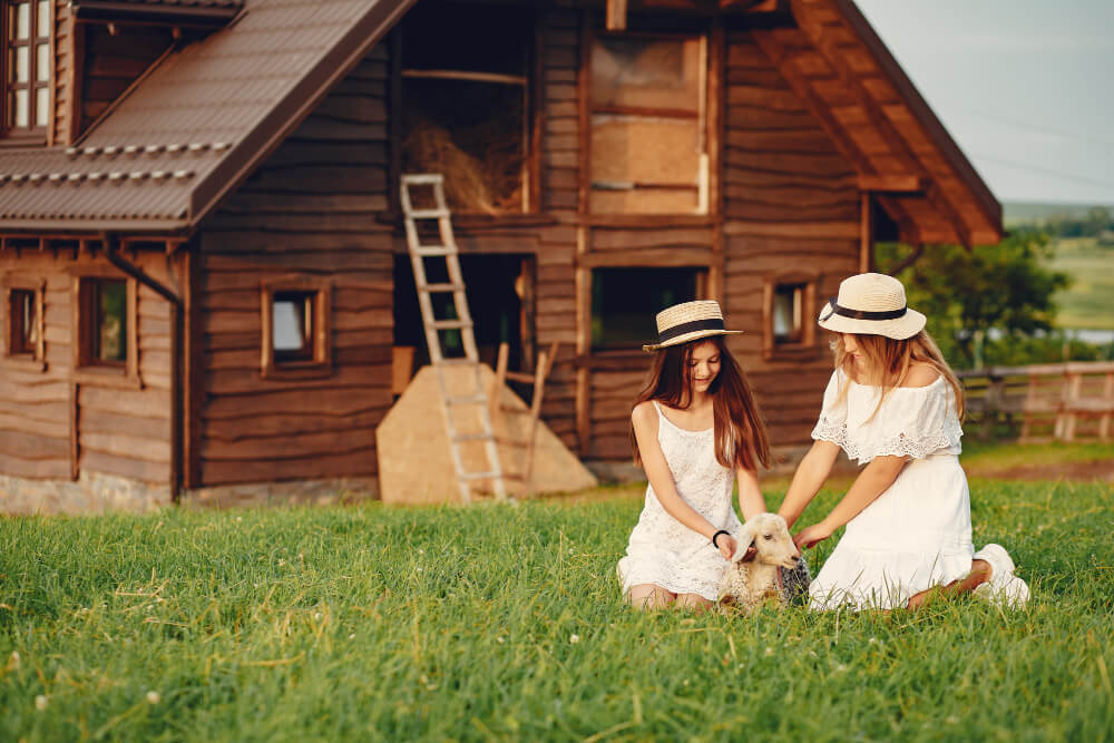 Mother and daughter sitting on the grass with a small lamb in front of a family cottage, symbolizing passing a cottage to the next generation, with estate planning guidance from TLR Law in Manitoba.