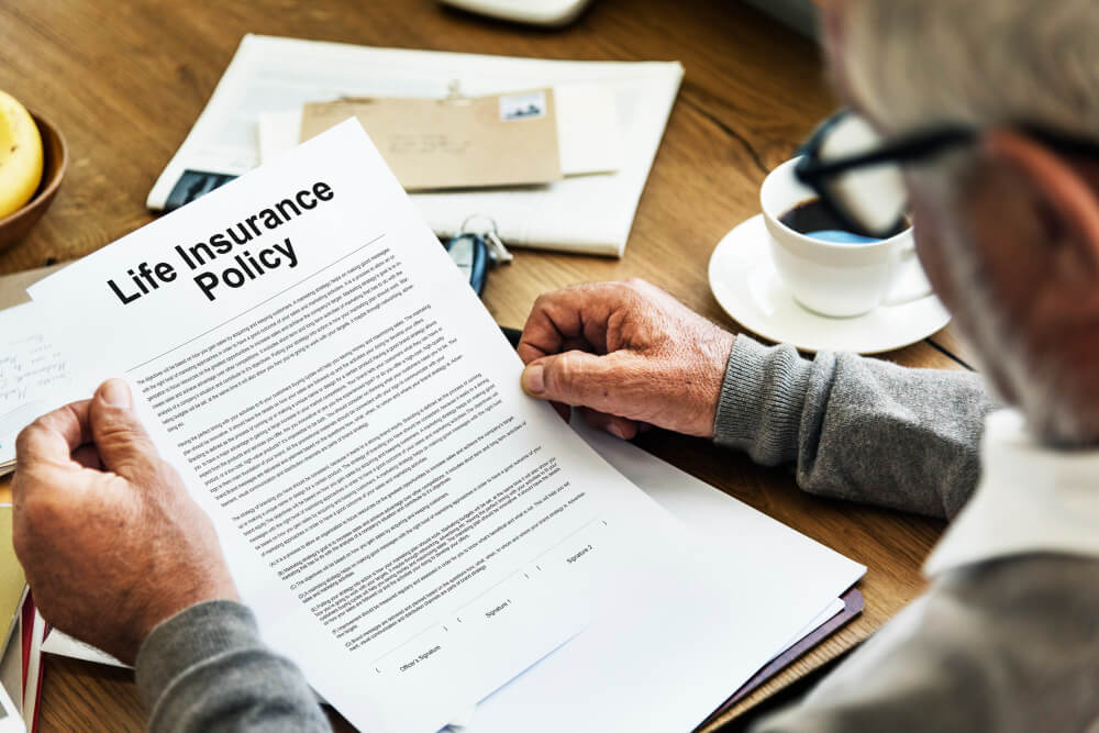 Man reviewing a life insurance policy document at a table, highlighting the importance of beneficiary designations for RRSPs and insurance with estate planning guidance from TLR Law in Manitoba.