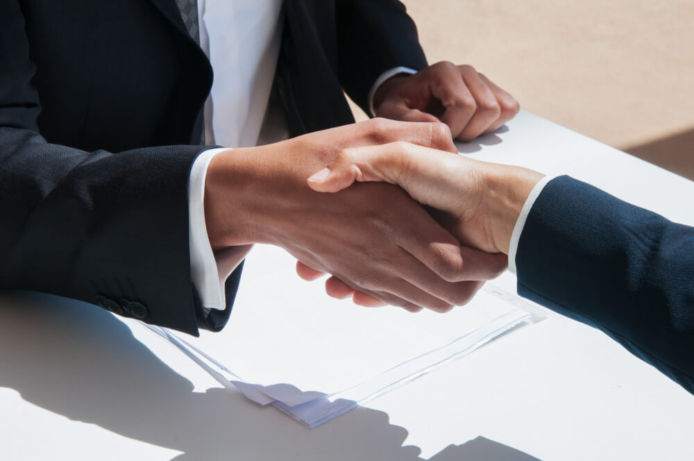 Two business partners shaking hands over documents, symbolizing shareholder agreements and business partnership planning with legal guidance from TLR Law in Manitoba.