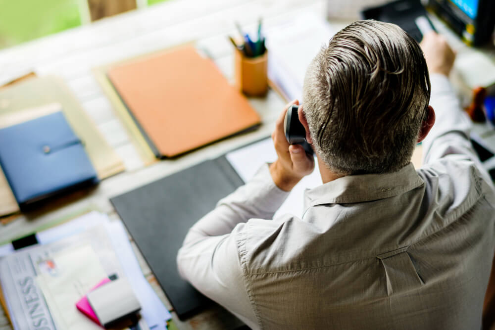 Man speaking on the phone at his desk reviewing documents, representing a real estate discovery call for quick legal guidance with TLR Law in Manitoba.