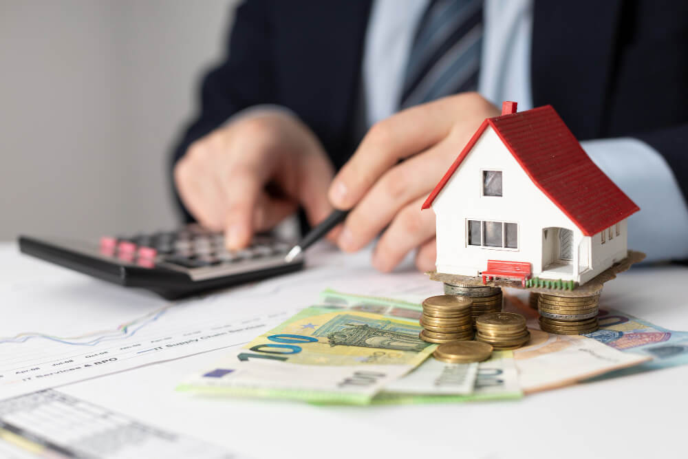 Small house model, Canadian money, coins, and calculator representing estate value and bank requirements for wills, with estate planning guidance from TLR Law in Manitoba.