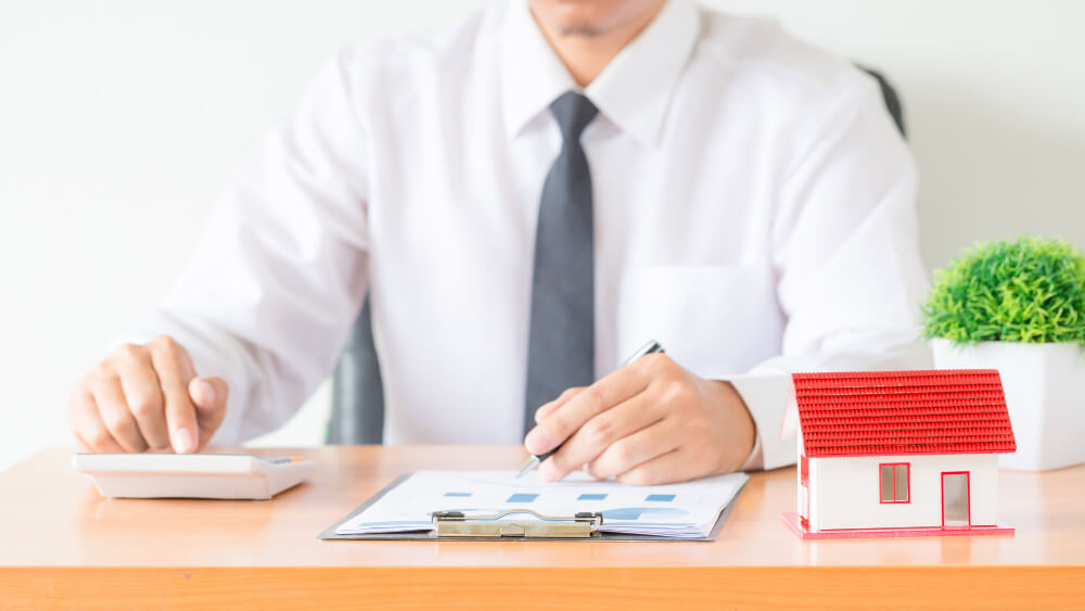 Real estate professional reviewing purchase documents beside a house model, representing legal steps for Manitoba homebuyers with guidance from TLR Law in Manitoba.