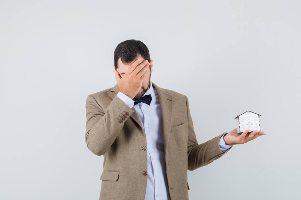 Stressed homeowner holding a miniature house model, representing concerns over property fraud, survey issues, and title insurance protection with guidance from TLR Law in Manitoba.