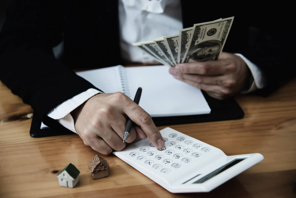Business owner reviewing finances with cash, calculator, and a model house, representing business assets and estate planning with TLR Law in Manitoba.