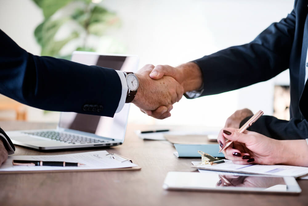Business professionals shaking hands over documents, representing business continuity planning, legal authority, and corporate succession with TLR Law in Winnipeg, Manitoba.