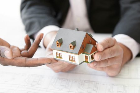 Hands holding a model house during property discussion, symbolizing joint ownership, estate planning, and protecting real estate assets in Manitoba with TLR Law.