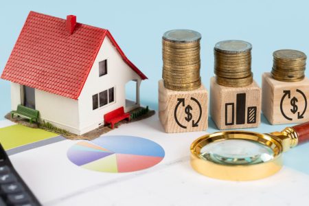 Model house beside stacked coins, financial charts, and a magnifying glass symbolizing asset division and property rights for common-law couples, with legal guidance from TLR Law in Manitoba.
