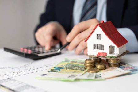 Small house model, Canadian money, coins, and calculator representing estate value and bank requirements for wills, with estate planning guidance from TLR Law in Manitoba.