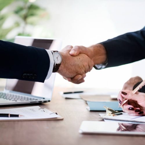 Business professionals shaking hands over documents, representing business continuity planning, legal authority, and corporate succession with TLR Law in Winnipeg, Manitoba.