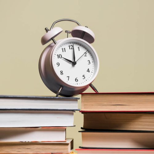 Alarm clock resting on stacked books, representing corporate recordkeeping deadlines and minute book maintenance for TLR Law in Manitoba.