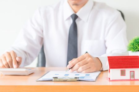 Real estate professional reviewing purchase documents beside a house model, representing legal steps for Manitoba homebuyers with guidance from TLR Law in Manitoba.