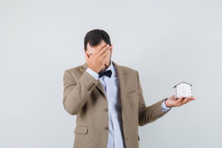 Stressed homeowner holding a miniature house model, representing concerns over property fraud, survey issues, and title insurance protection with guidance from TLR Law in Manitoba.