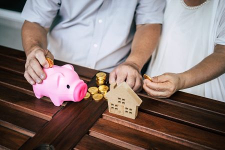 Couple saving money beside a house model and piggy bank, illustrating how a home and savings are distributed without a will, with estate planning guidance from TLR Law in Manitoba.