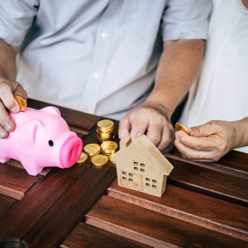 Couple saving money beside a house model and piggy bank, illustrating how a home and savings are distributed without a will, with estate planning guidance from TLR Law in Manitoba.