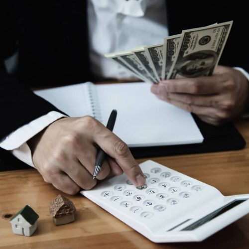 Business owner reviewing finances with cash, calculator, and a model house, representing business assets and estate planning with TLR Law in Manitoba.