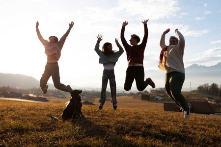 A joyful blended family jumping together outdoors at sunset, symbolizing unity and happiness. A dog sits in the foreground, adding warmth to the scene. This represents the importance of estate planning to protect loved ones in blended families.