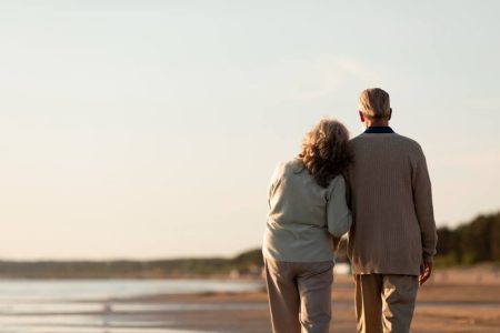 An elderly couple walking together along a quiet beach at sunset, symbolizing reflection, values, and legacy planning for future generations.