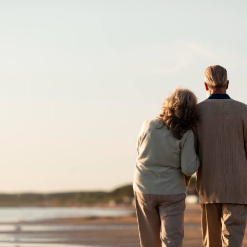 An elderly couple walking together along a quiet beach at sunset, symbolizing reflection, values, and legacy planning for future generations.